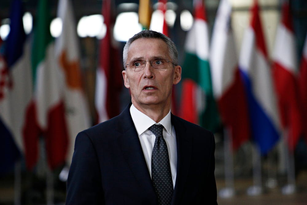 Jens Stoltenberg standing in front of flags