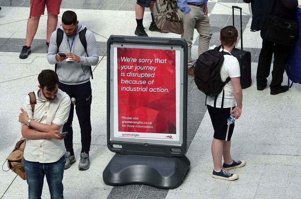 People stand around a red sign reading: We're sorry your journey is disrupted because of industrial action