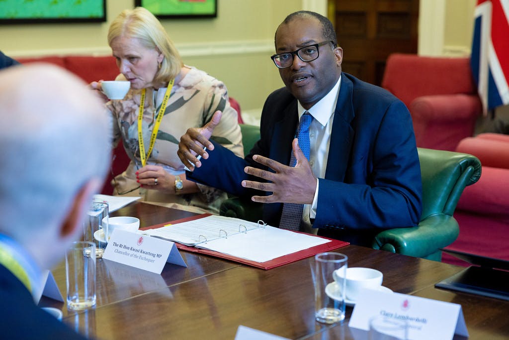 Kwasi Kwarteng sits at a table and speaks to officials