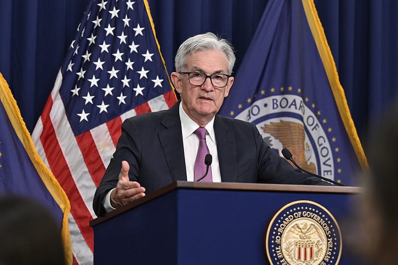Jerome Powell stands at a lectern in front of American and Federal Reserve flags