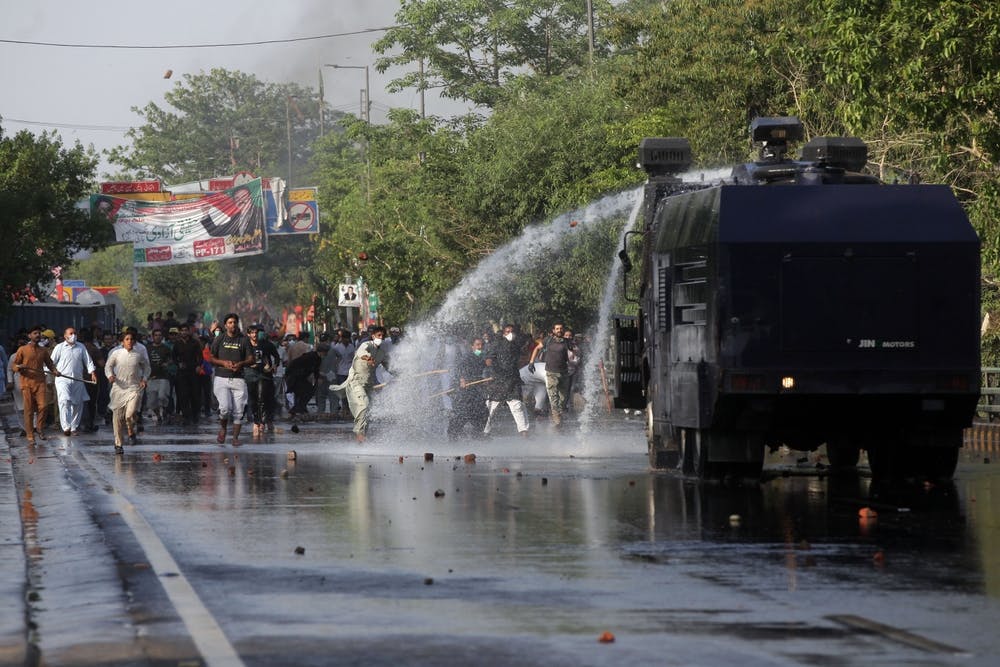 Supporters of Imran Khan throw stones at a police water cannon in Lahore
