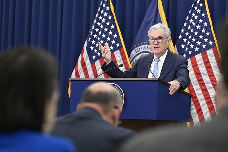 Jerome Powell stands at a podium in front of American and Fed flags