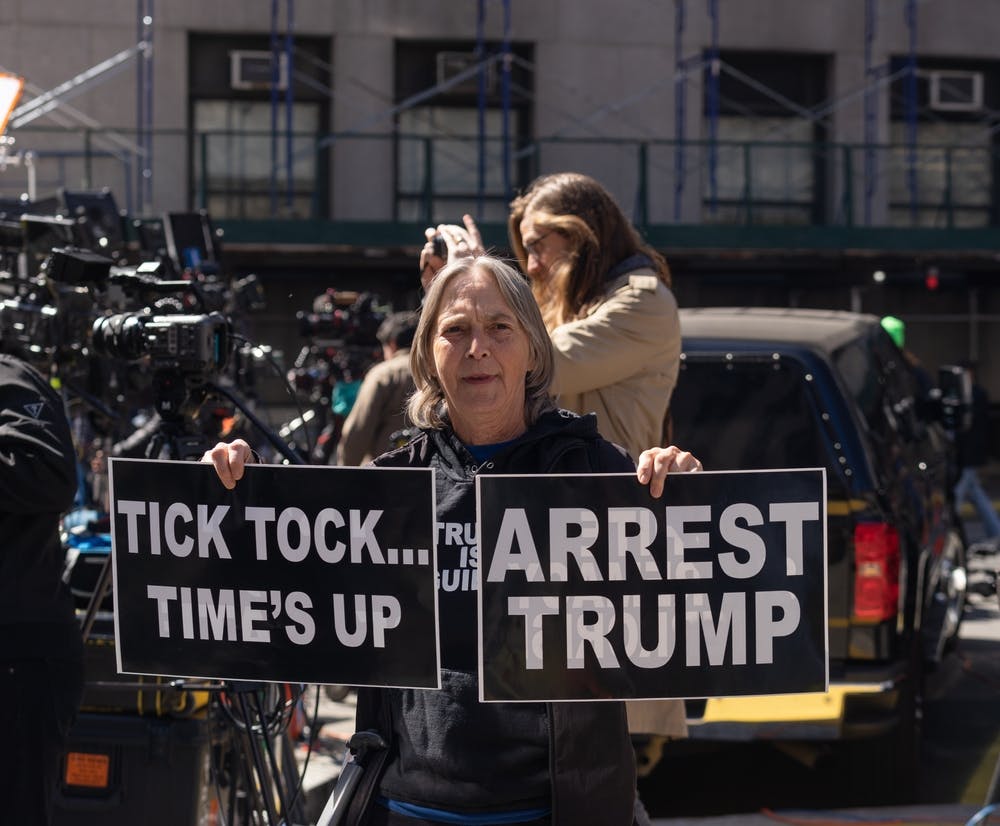 protester holds signs reading Tick tock...time's up and arrest trump