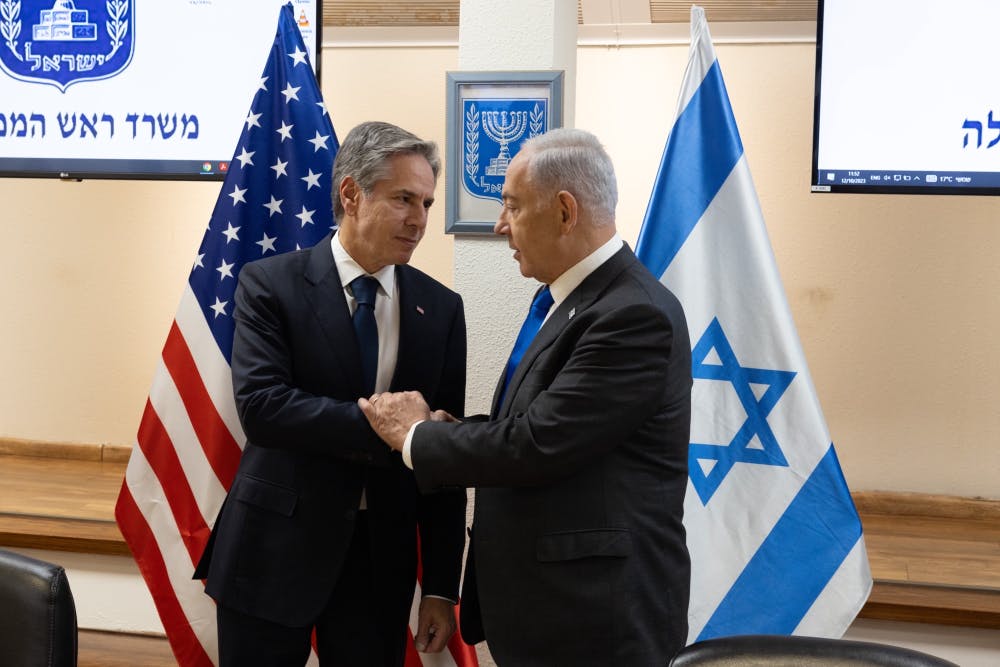 Antony Blinken shakes hands with Benjamin Netanyahu in front of American and Israeli flags