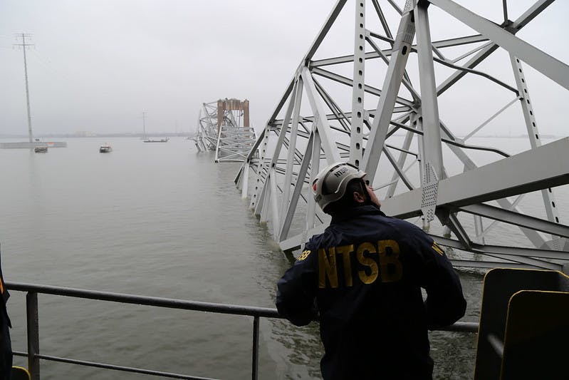 NTSB staff stand on a ship in front of the collapsed Key Bridge