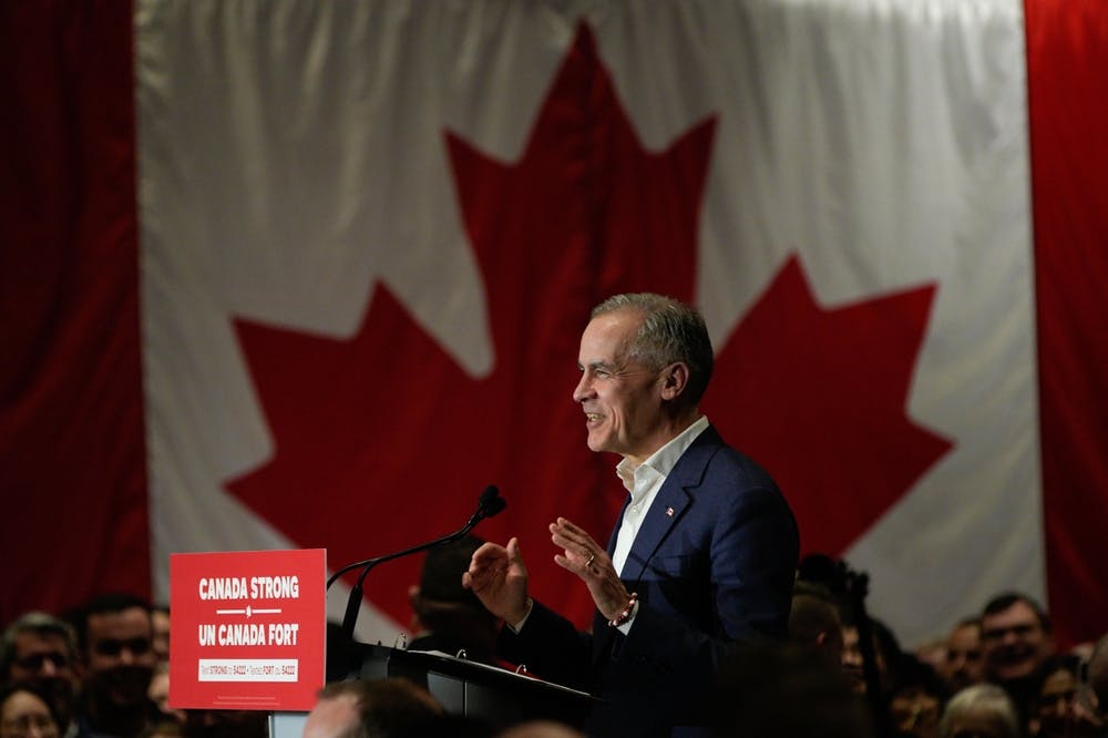 Mark Carney stands at a podium in front of a Canadian flag with a sign reading Canada Strong