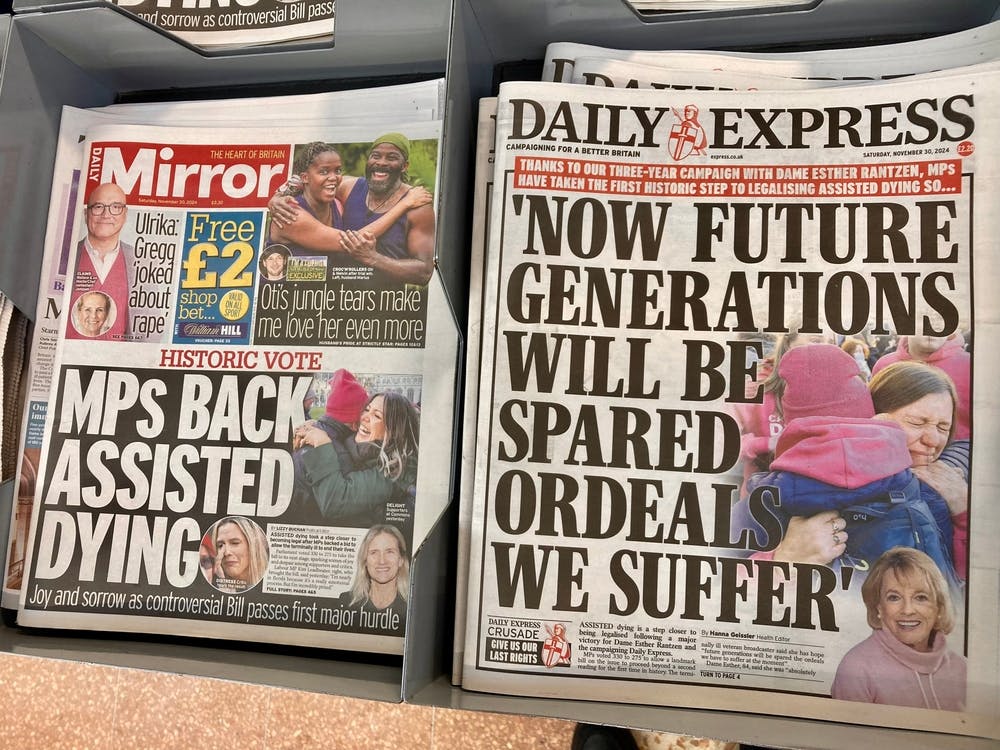 Mirror and Daily Express newspapers sit next to each other on a newsstand, featuring splash headlines about assisted dying. The Mirror reads: MPs back assisted dying. The Daily Express reads: Now future generations will be spared ordeal we suffer