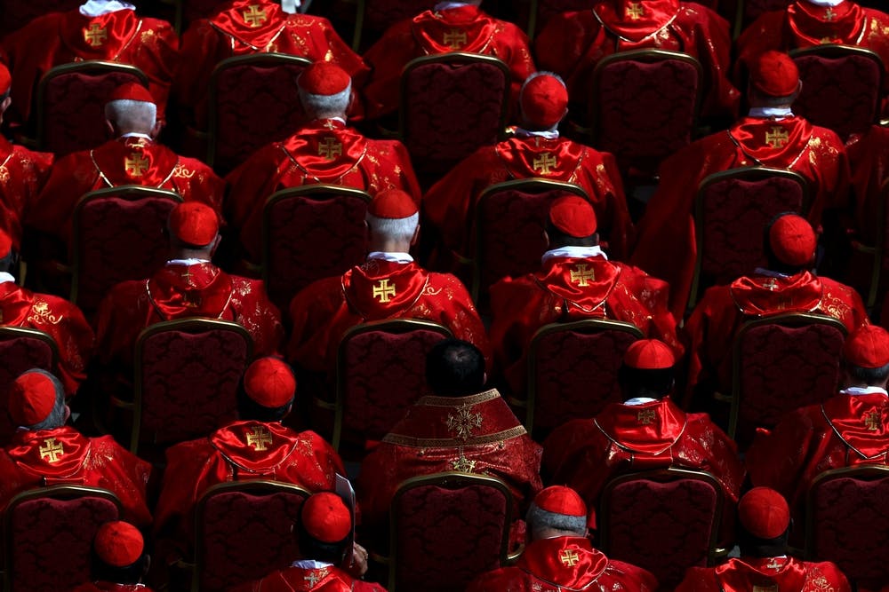 Cardinals dressed in red robes and hats sit in the churchyard at the funeral of Pope Francis