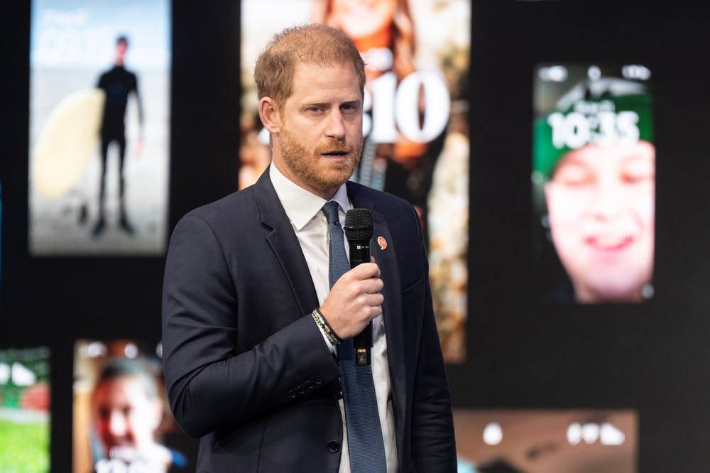 Prince Harry speaks into a microphone in front of photos of children