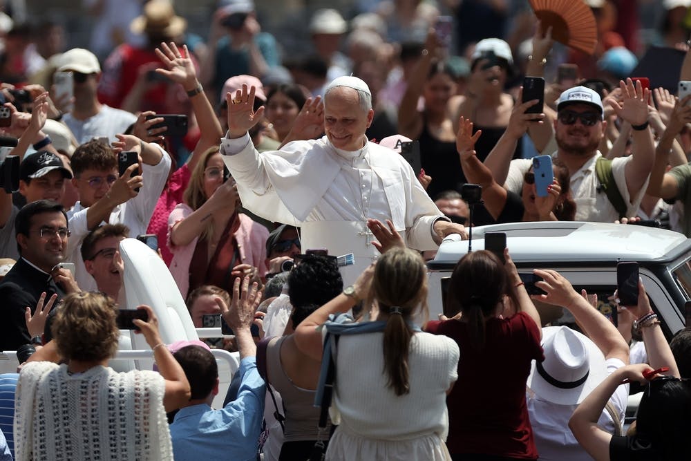 Pope Leo travels through a crowd, waving from a car